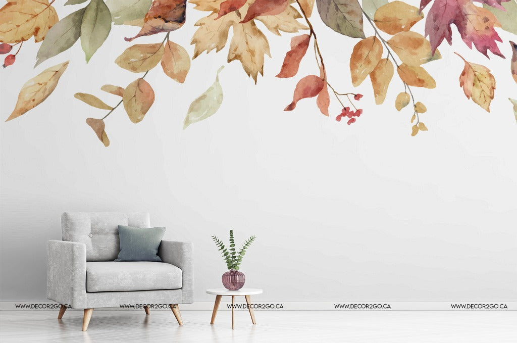 A modern minimalist living room with a gray armchair and a small round table with a potted plant. The wall behind is adorned with large, colorful Falling Leaves Wallpaper Mural decals from Decor2Go Wallpaper Mural.