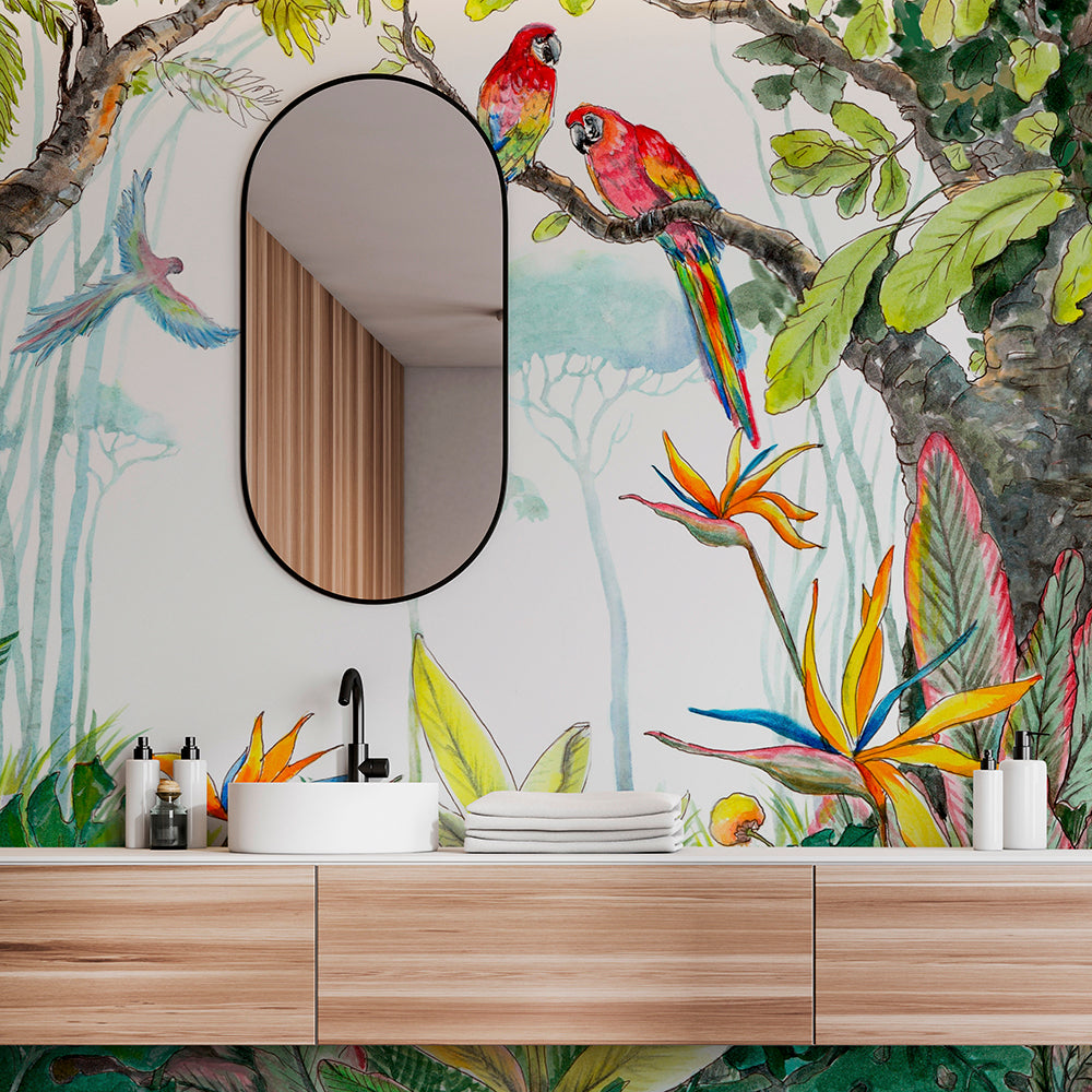 A vibrant bathroom with an oval mirror above a wooden vanity. The wall features lush, colorful Escape to the Jungle Wallpaper Mural from Decor2Go Wallpaper Mural of a watercolor forest with parrots, hummingbirds, and exotic flowers.