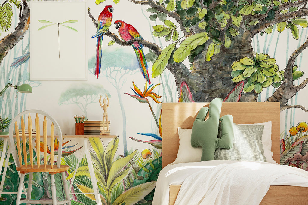 A vibrant bedroom with Decor2Go Wallpaper Mural's Escape to the Jungle Wallpaper Mural depicting a watercolor forest and colorful birds. A wooden chair and desk sit beside a bed with white linens and green pillows.