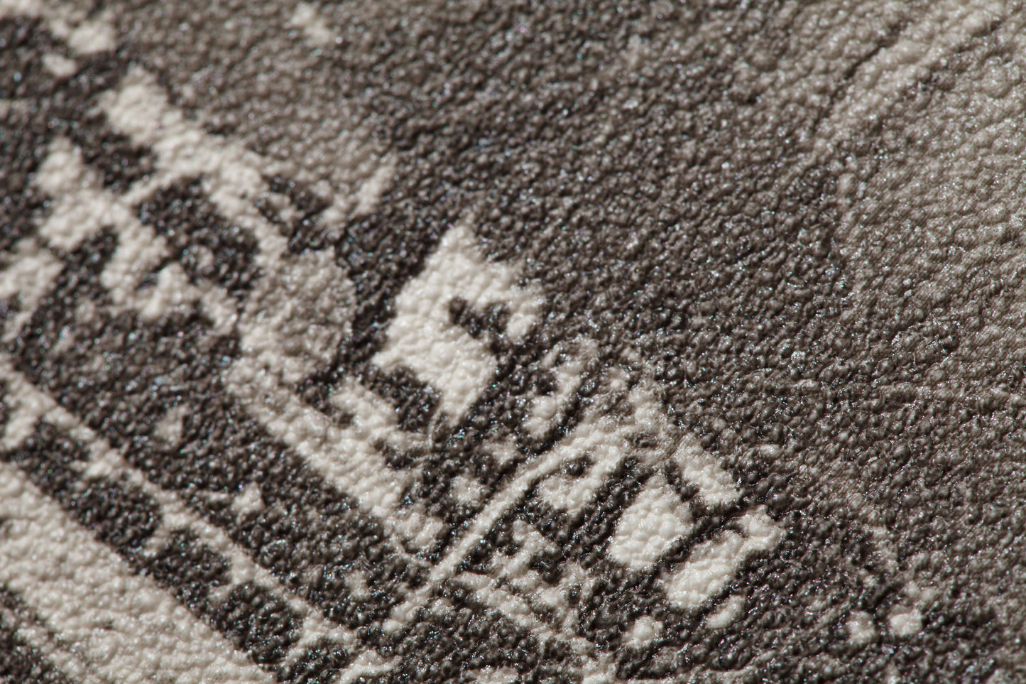 Close-up of a textured, black-and-white image on a surface. The slightly pixelated scene pattern shows abstract shapes and patterns, making it difficult to discern specific details or objects. The texture resembles a grainy or rough finish, evoking the feel of Palitra Voyage Wallpaper (114 SqFt).