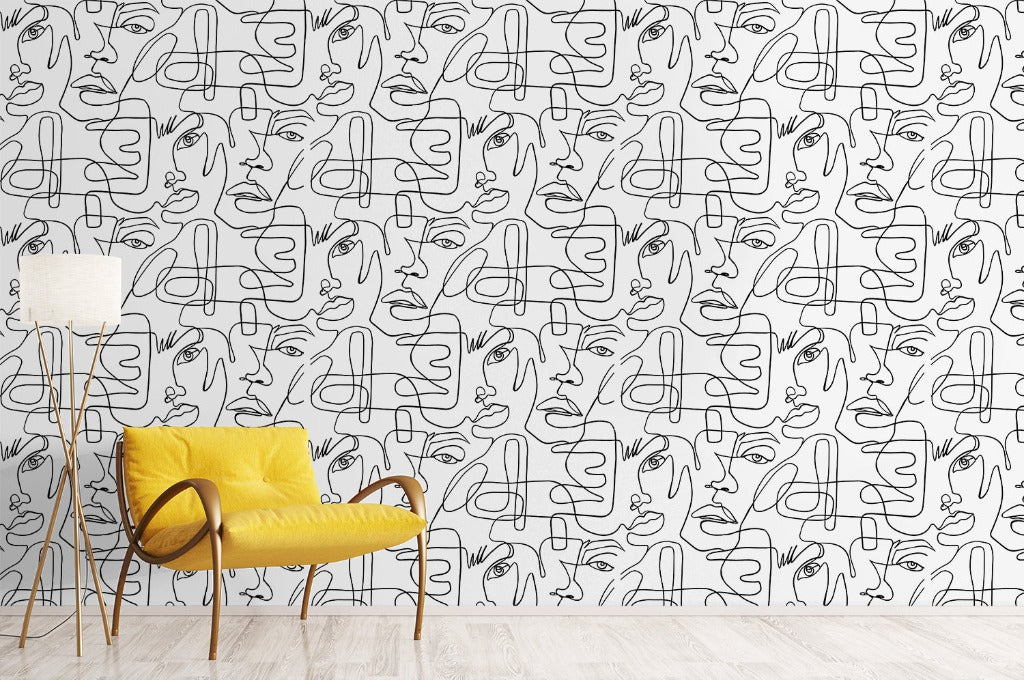 A modern living room with a vibrant yellow armchair and a standing lamp on a wooden floor. The wall behind is covered with One Line Portraits Wallpaper Mural from Decor2Go Wallpaper Mural, featuring abstract faces, adding a creative touch to the space.