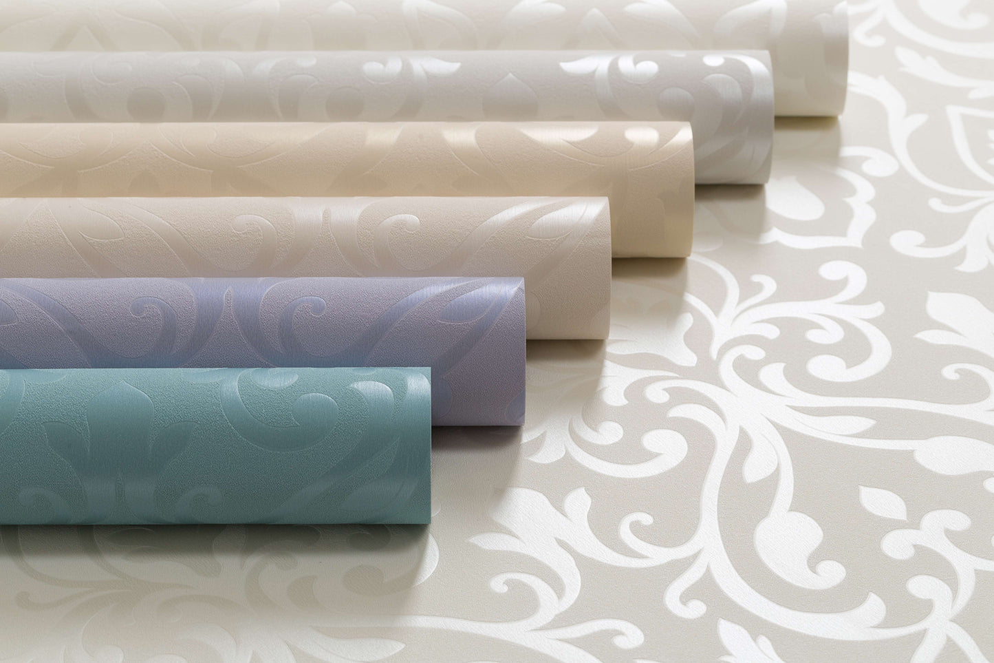 Various rolls of Rhodonis Wallpaper (114 SqFt) by Palitra in soft pastel colors (white, beige, blue, and light green) are displayed on a flat surface. Each roll features an elegant, hot stamping embossed floral pattern that adds a textured, decorative element to the modern design.