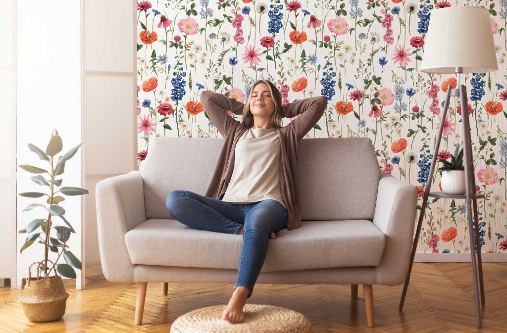A woman relaxing on a sofa with her arms behind her head, smiling contentedly in a cozy living room with Decor2Go Wallpaper Mural's Floral Summer Wallpaper Mural and a stylish lamp.