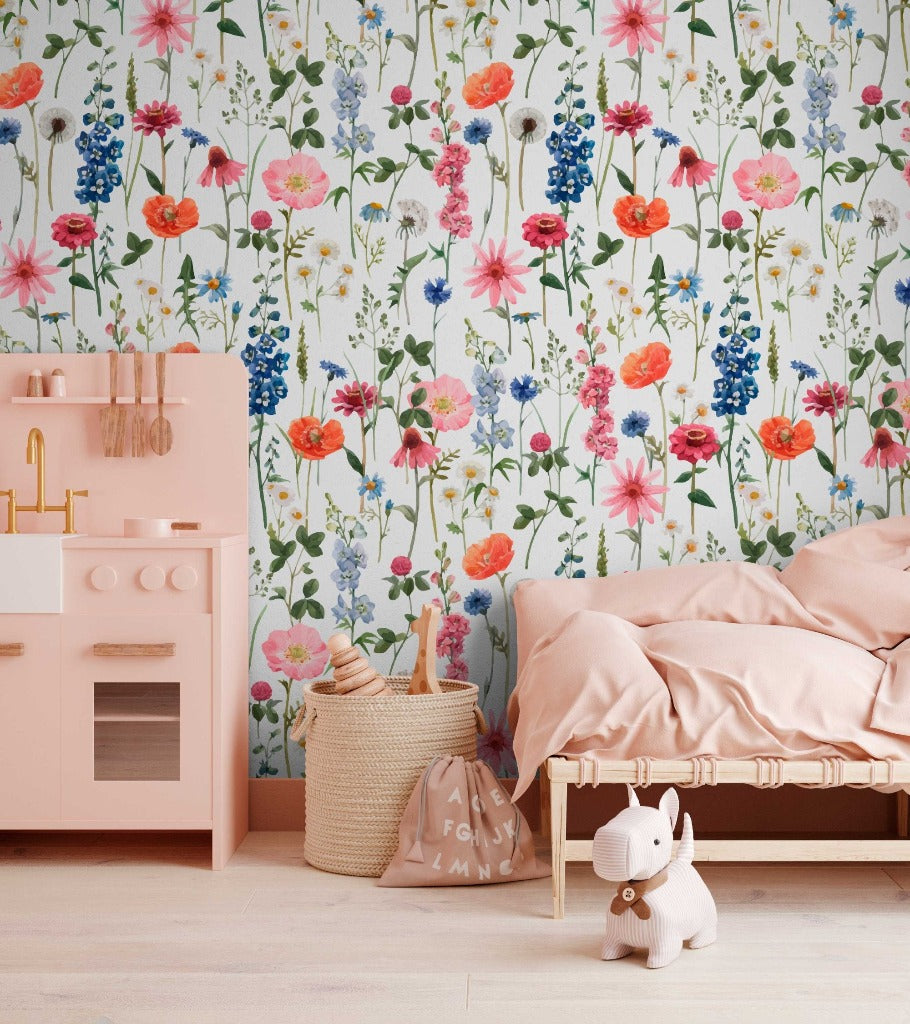A colorful, Floral Summer Wallpaper Mural from Decor2Go Wallpaper Mural in a child's room with a wooden bed draped in pink bedding, a pink play kitchen, two woven baskets, and a white toy unicorn on the floor creates a.