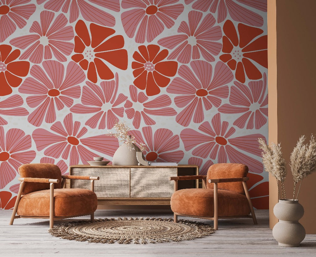A cozy living room corner featuring two plush orange armchairs, a beige sofa, and a circular rug. The room is accented by a bold custom mural depicting Groovy Flowers Wallpaper Mural in shades of orange and yellow.