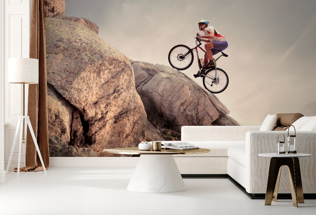 A surreal image depicting a living room with a mountain biker jumping between rocks, integrated into a Decor2Go Wallpaper Mural behind a modern sofa and coffee table.