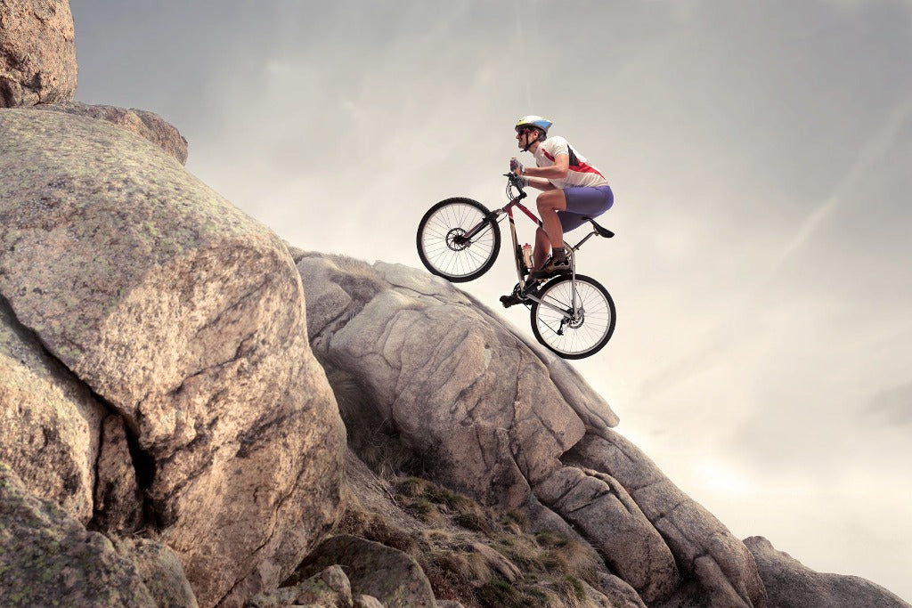 A cyclist in a white helmet and purple outfit skillfully rides a Decor2Go Wallpaper Mural mountain bike down a steep, rocky incline under a cloudy sky, embodying the spirit of extreme sports.