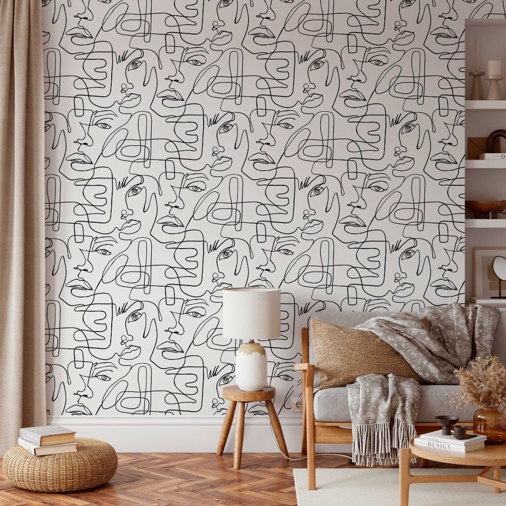 Cozy living room corner with a stylish lamp on a small table, a plush sofa with a gray throw, and a patterned wall with Decor2Go Wallpaper Mural of One Line Portraits.