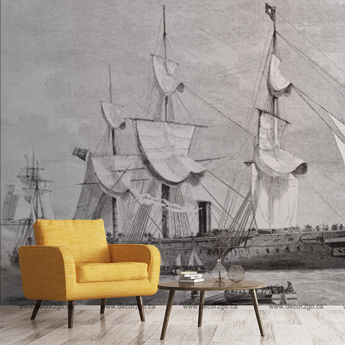 A modern living room with a bright orange armchair and a small wood table, in front of a large black and white mural of Decor2Go Wallpaper Mural sailing ships, inspired by classic pirate stories.
