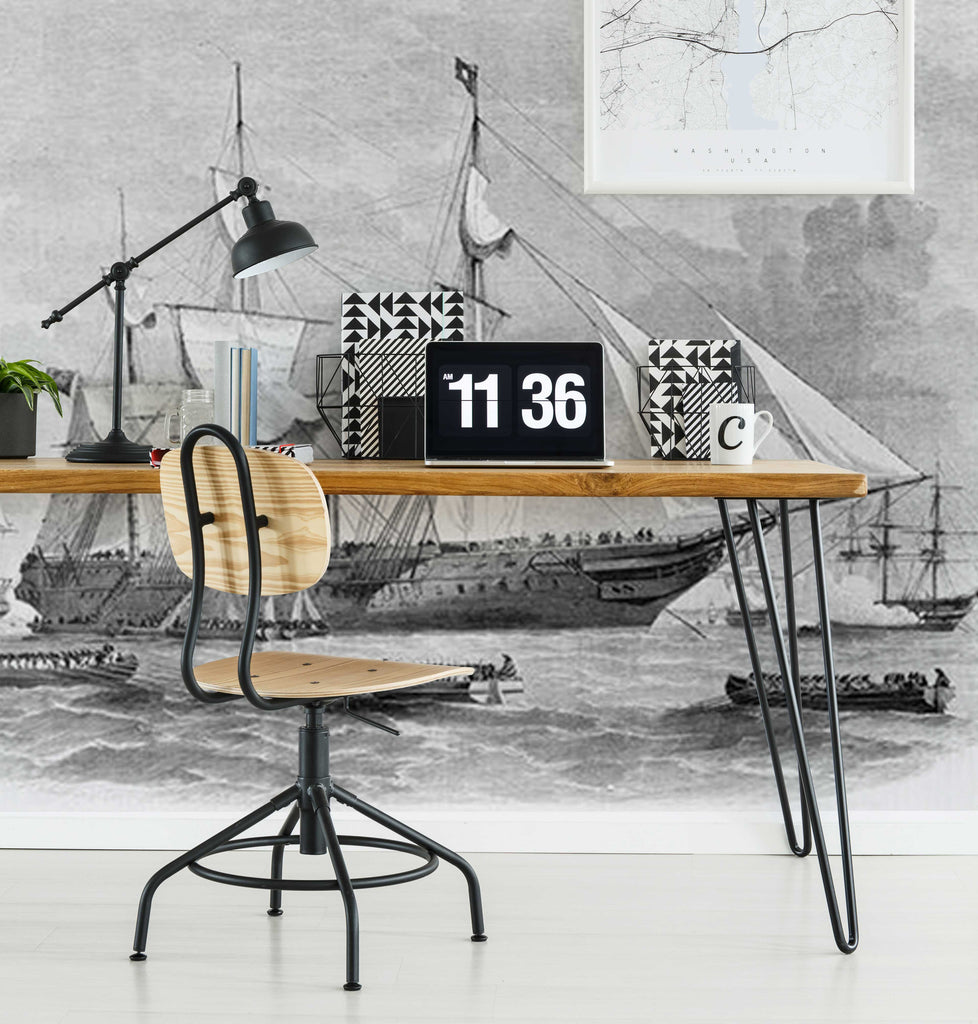 A stylish home office featuring a wooden desk with hairpin legs, a laptop displaying the time, a potted plant, and books. Decor2Go's Sailing Away Wallpaper Mural provides a nautical vibe.