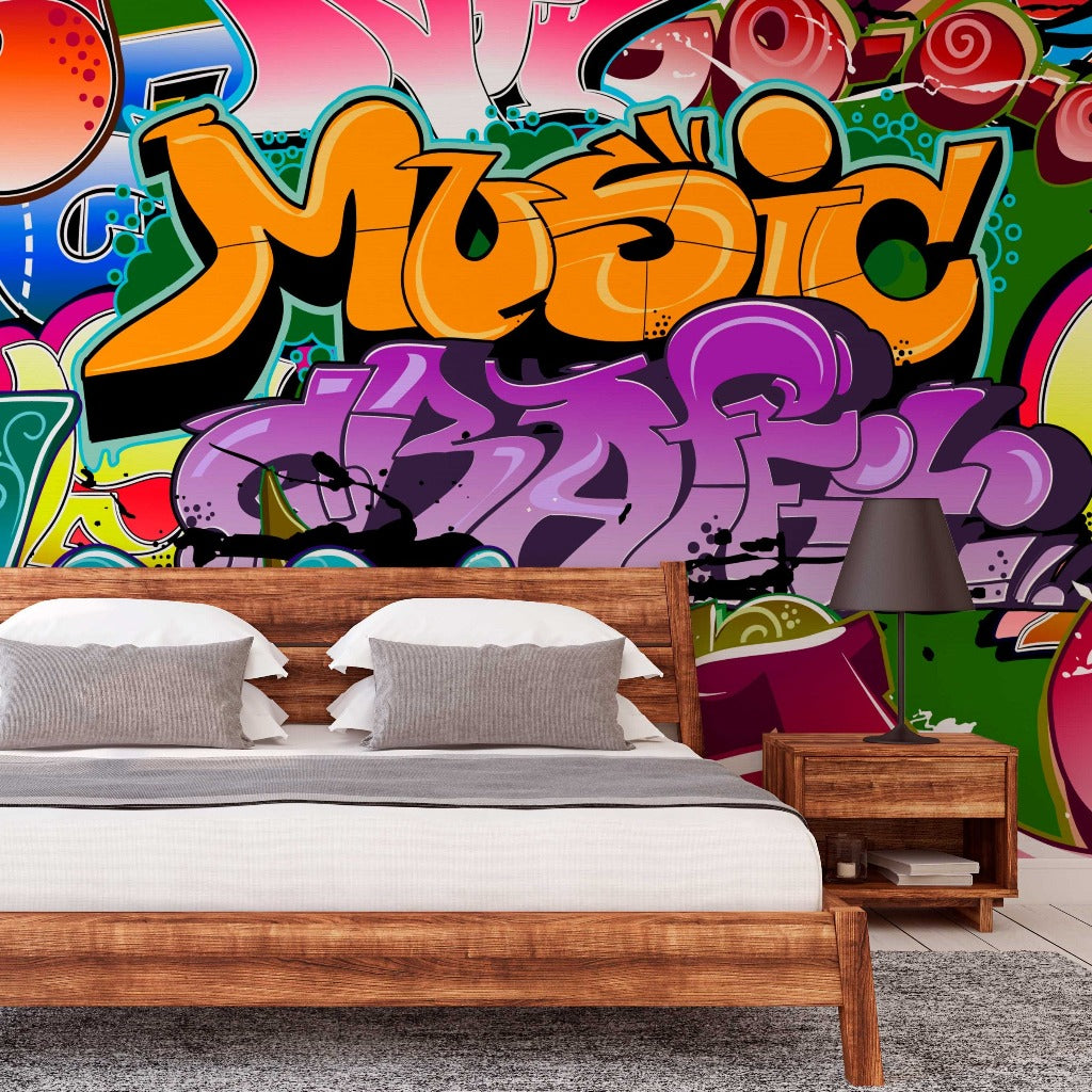 A modern bedroom featuring a large, colorful Decor2Go Urban Colors wallpaper mural with the word "music" prominently displayed. The room includes a wooden bed with white bedding and a matching nightstand.