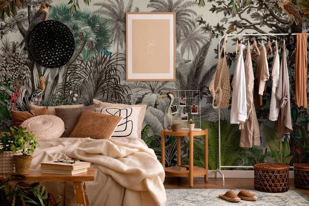 A cozy bedroom corner with a Vintage Jungle Wallpaper Mural by Decor2Go Wallpaper Mural featuring birds and dense foliage, a neatly made bed, a small wooden stool, hanging clothes, and various plants enhancing the room’s natural vibe.