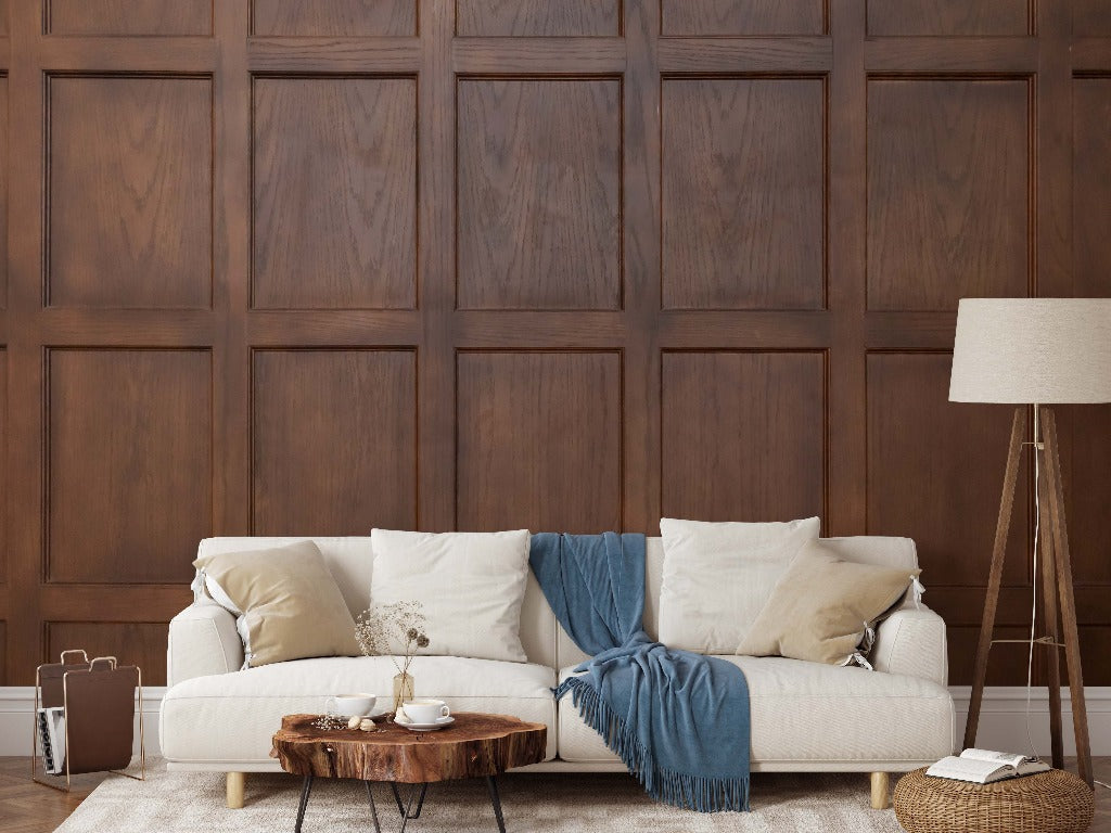 A cozy living room setup with a white sofa adorned with neutral-toned cushions and a blue throw, a wooden floor lamp, and a coffee table with books and a tray, against Decor2Go Wallpaper Mural.