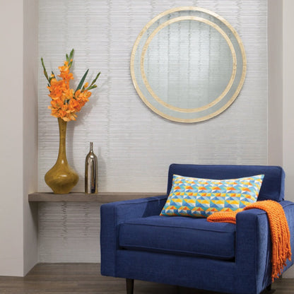 A contemporary living room corner showcases a blue armchair embellished with a geometric-patterned pillow and an orange throw. In the backdrop, tall yellow and metallic vases are set against a wall adorned with York Wallcoverings' Split Levels Wallpaper (60 SqFt). The space is further enhanced by a round mirror, adding the perfect modern decor flair.