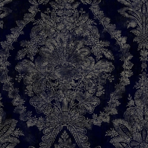 Charleston Damask Elegant Wallpaper by York Wallcoverings transforms ornate dark blue fabric into a masterpiece, featuring silver floral and leafy designs. It showcases detailed flower motifs and curved foliage for a sophisticated, symmetrical look. Available in 60 SqFt rolls.