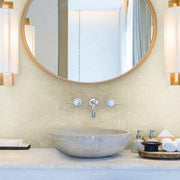 Bathroom - A modern features a round mirror with a wooden frame, two mounted lights on each side, and a stone basin sink with a wall-mounted faucet. The sink area includes a tray with toiletries and a white washcloth. The wall boasts York Wallcoverings' Geodes Layers Wallpaper (60 SqFt) for added sophistication