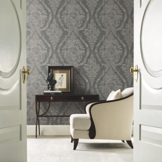 A white armchair sits beside a dark wooden console table against the Charleston Damask Wallpaper (60 SqFt) by York Wallcoverings. A framed artwork and a small bust are placed on the table. The scene is viewed through open double doors with golden handles, radiating Southern affluence.