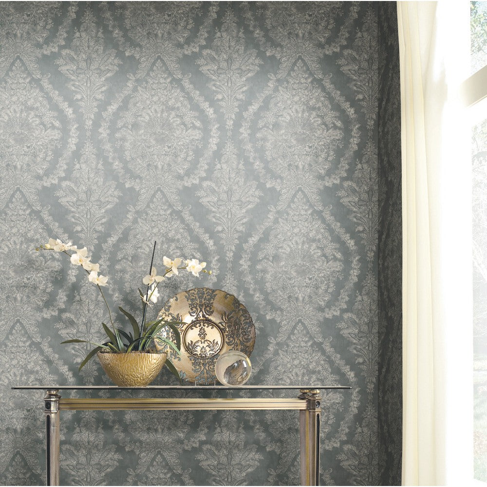 A small glass table holds a decorative golden bowl, a gold and black plate, and a white orchid plant. The background displays York Wallcoverings' Grey Charleston Damask Elegant Wallpaper, featuring classic floral motifs in muted blue and grey tones.