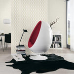 A modern, white egg-shaped chair with red interior cushioning stands on a black rug in a contemporary living space. Behind it, a bookshelf with decor items is set against an Ontario Diamond Geometric (56 SqFt) wallpaper. The room is well-lit and features sleek, minimalistic furniture.